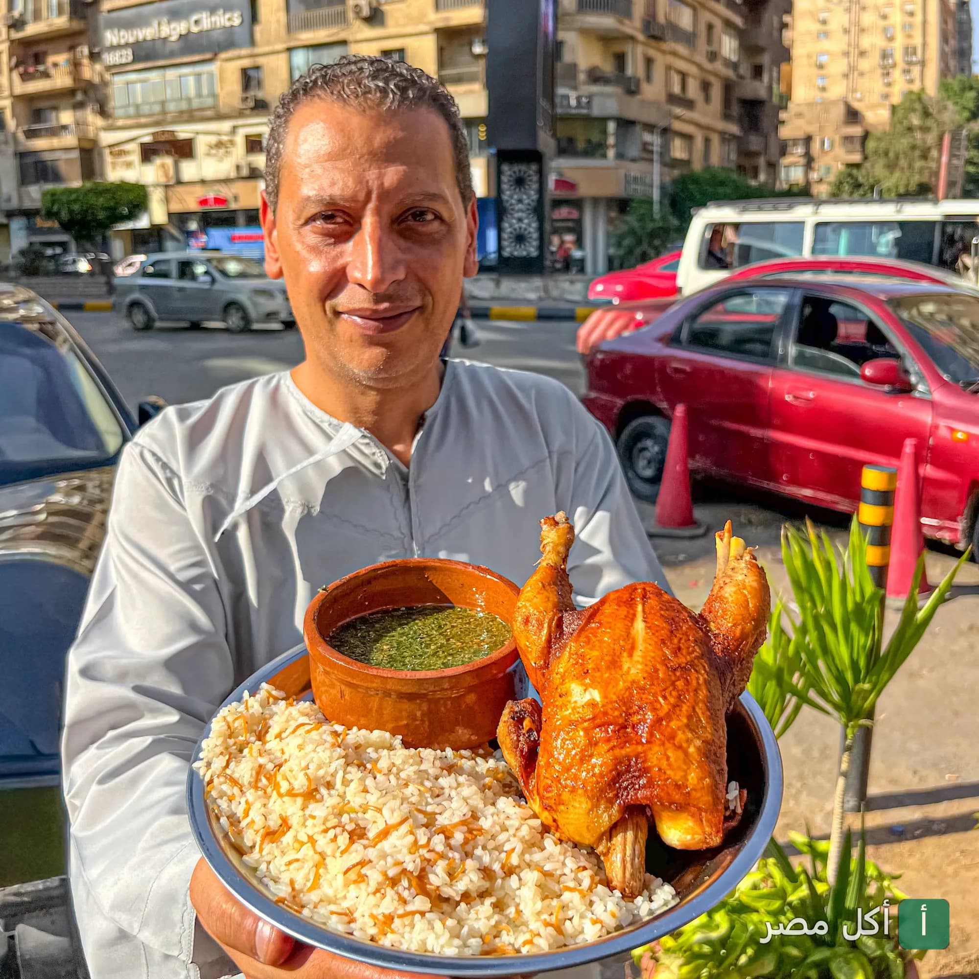 موظف مطعم دوار ام حسن بالدقي يقدم طبق دجاج محمر مع أرز بالشعيرية وملوخية في شارع حيوي.