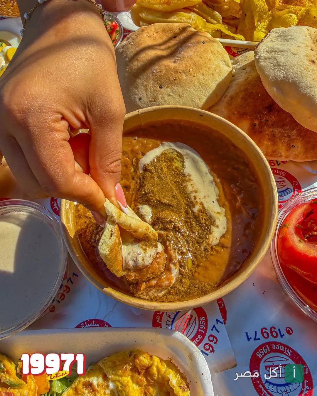 يد تغمس خبز بلدي في طبق فول مدمس مع طحينة في مطعم نجف بالصف.