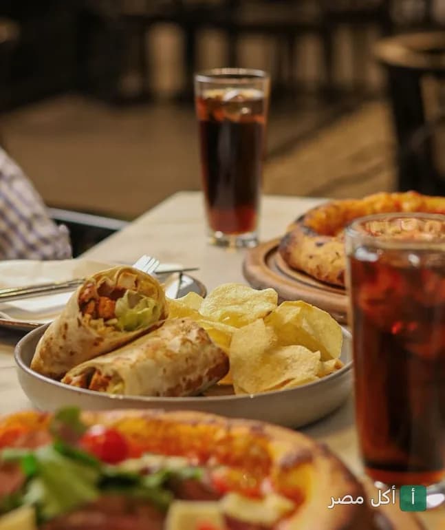 ساندوتشات شاورما مع بطاطس شيبسي وبيتزا على طاولة في مطعم استريا بالعطارين.