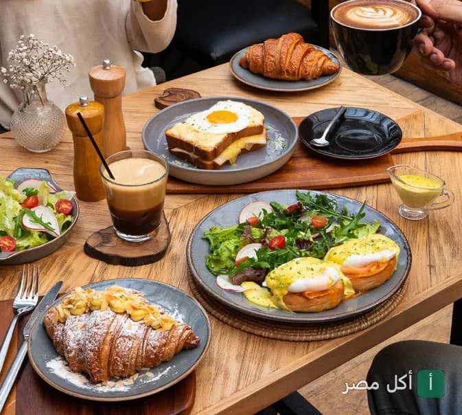 مائدة إفطار متنوعة في مطعم استريا بالعطارين، تضم بيض بينيديكت، كرواسون، وسلطة طازجة.