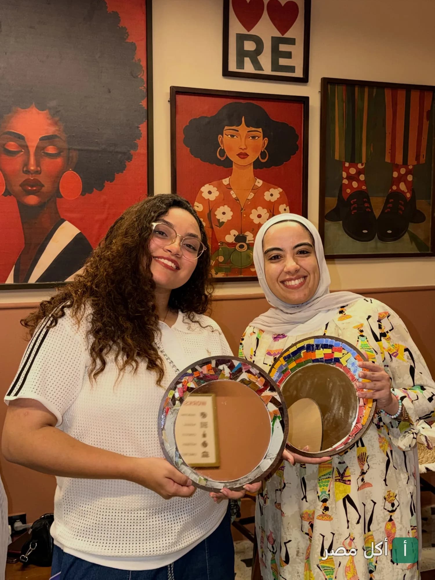 فتاتان تبتسمان وتحملان مرايا مزينة بقطع الموزاييك الملونة داخل مطعم فيراندا في منطقة العطارين بالإسكندرية.