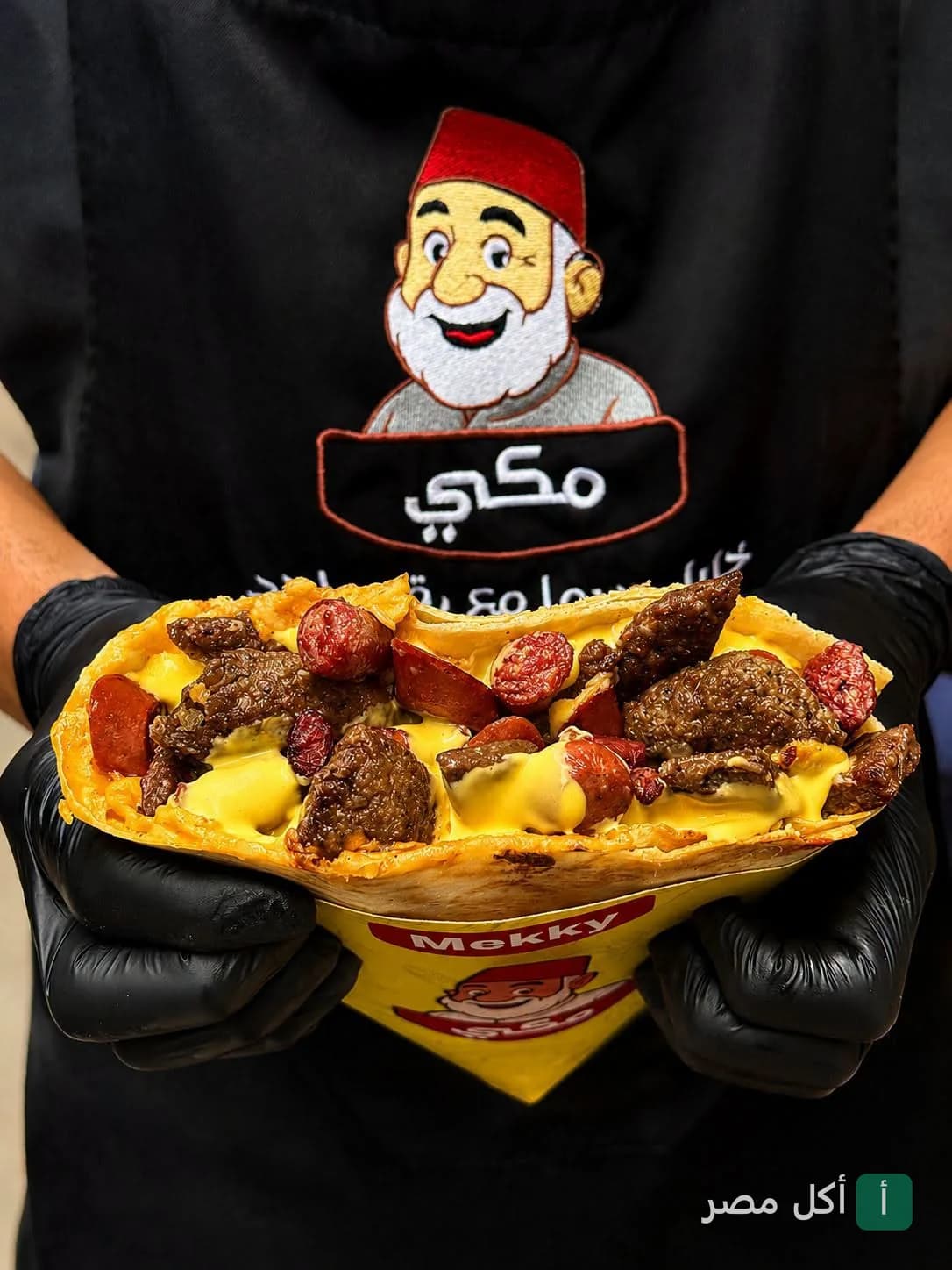 موظف يرتدي زي مطعم مكي يحمل ساندوتش كريب محشو باللحم والسجق والجبن الذائب.