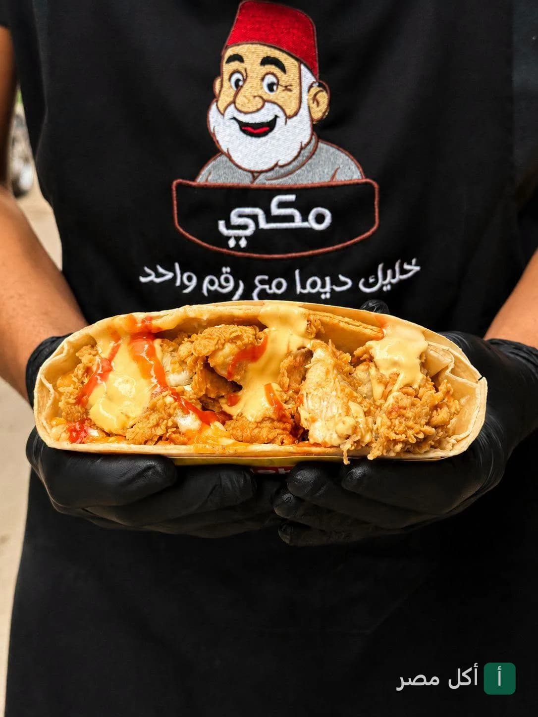 موظف يرتدي زي مطعم مكي يحمل ساندوتش كريب مقرمش بالدجاج والصوص في المنشية.