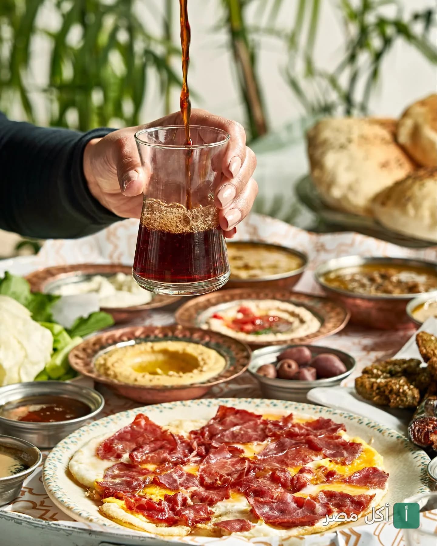 صب الشاي في كوب زجاجي على مائدة إفطار مصرية متنوعة في مطعم المحمدي بالمنشية.