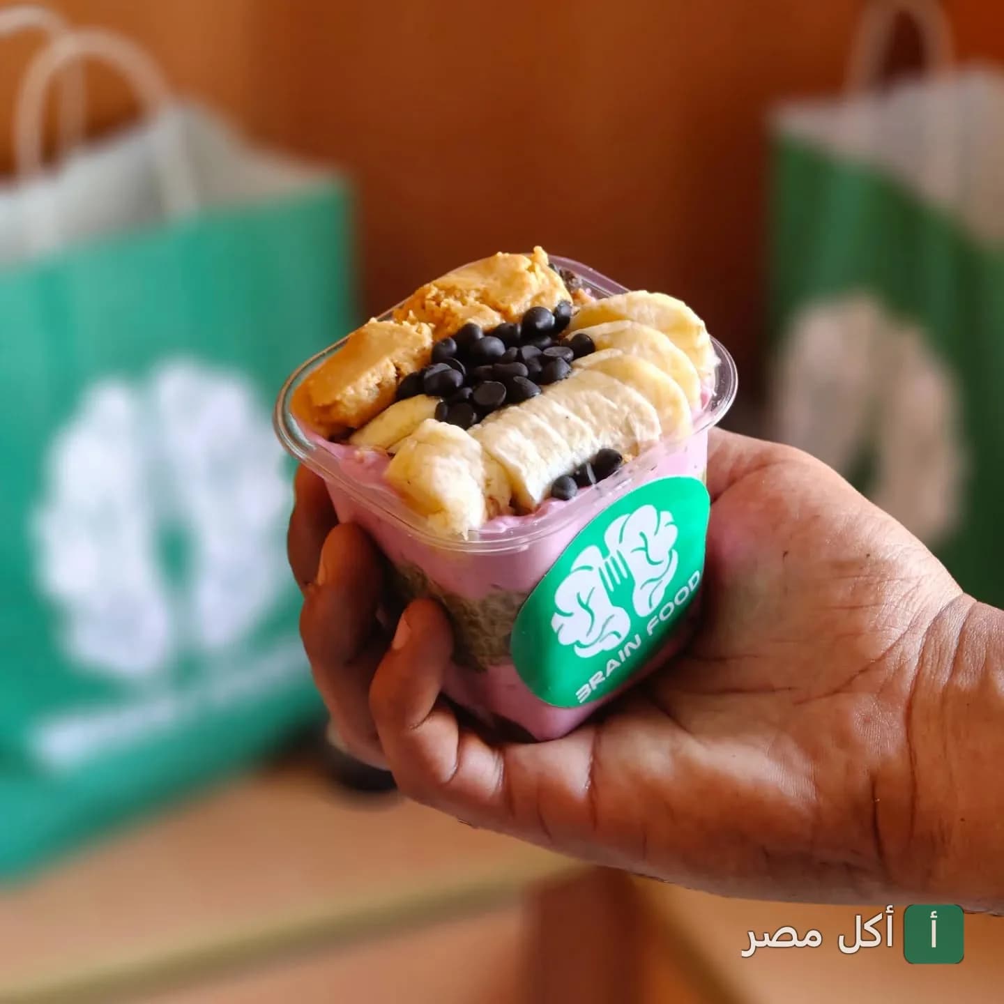 كوب سموذي من برين فود في الإسكندرية مزين بالموز وزبدة الفول السوداني وقطع الشوكولاتة.