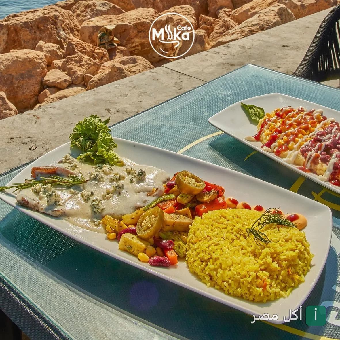 أطباق رئيسية متنوعة مع أرز أصفر وخضروات في كافيه ميكا بالإسكندرية بإطلالة بحرية.