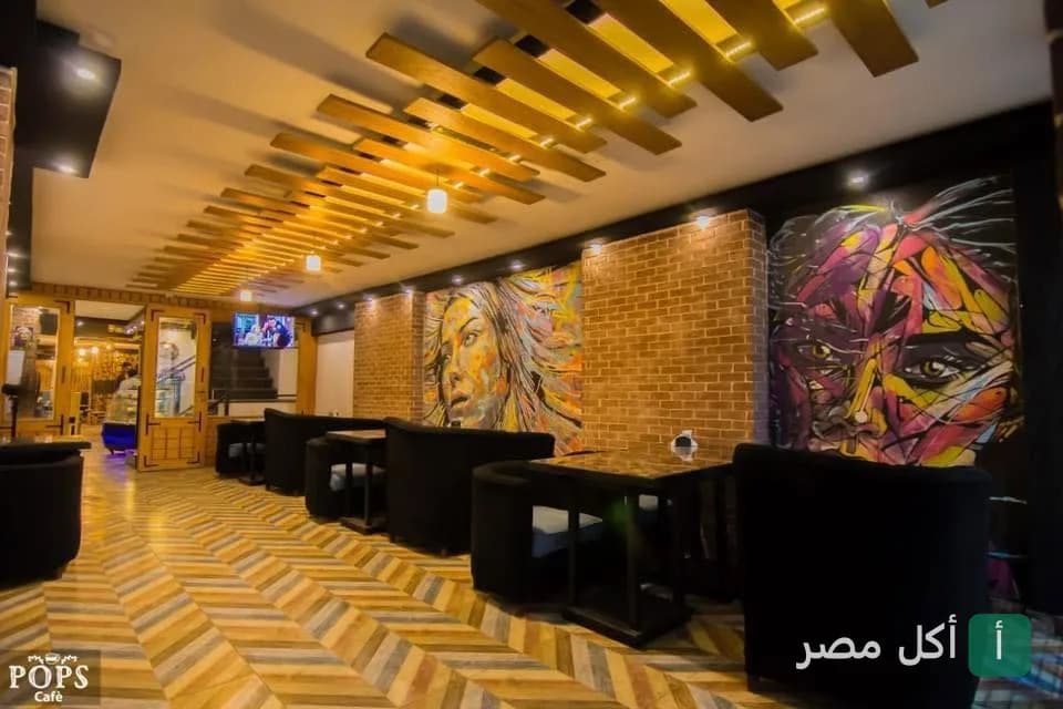 تصميم داخلي عصري في بوبس كافيه بسيدي بشر، يظهر جدران من الطوب مع رسومات فنية ومقاعد مريحة وإضاءة سقف خشبية.