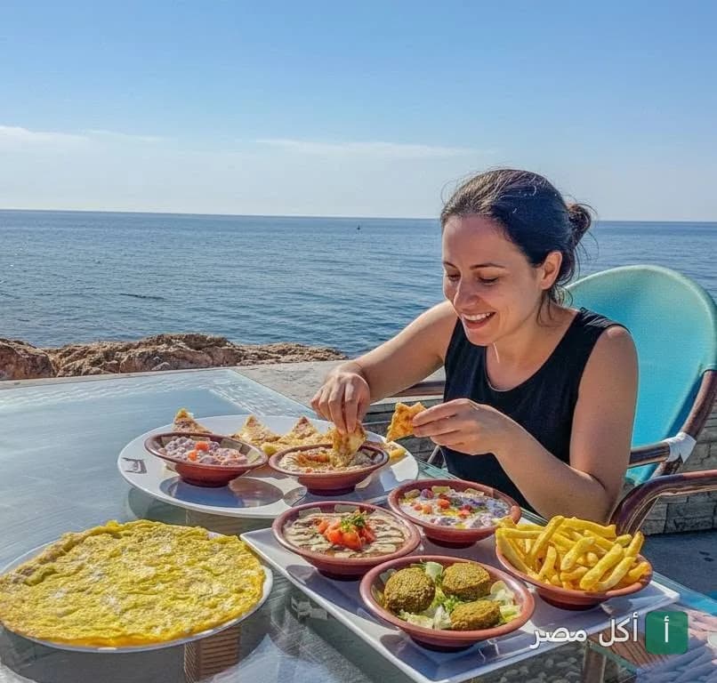 زبونة تتناول إفطاراً متنوعاً يضم الفول والفلافل والبيض أمام البحر في مطعم مورانو بالإسكندرية.
