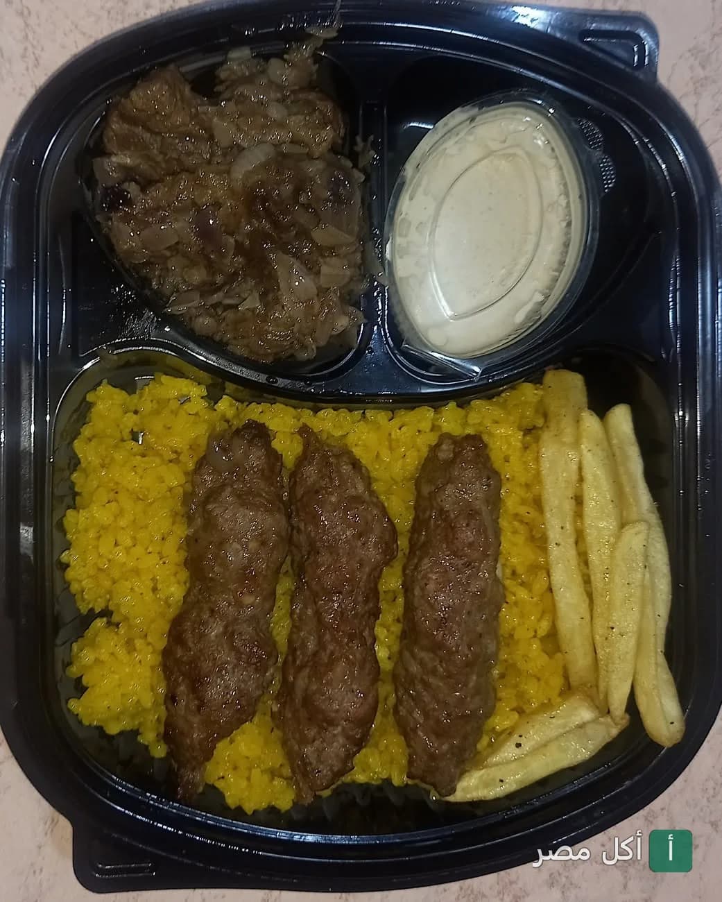 وجبة كفتة مشوية مع أرز أصفر وبطاطس محمرة وطحينة في علبة تيك أواي من مطعم قرية السمان ببرج العرب.
