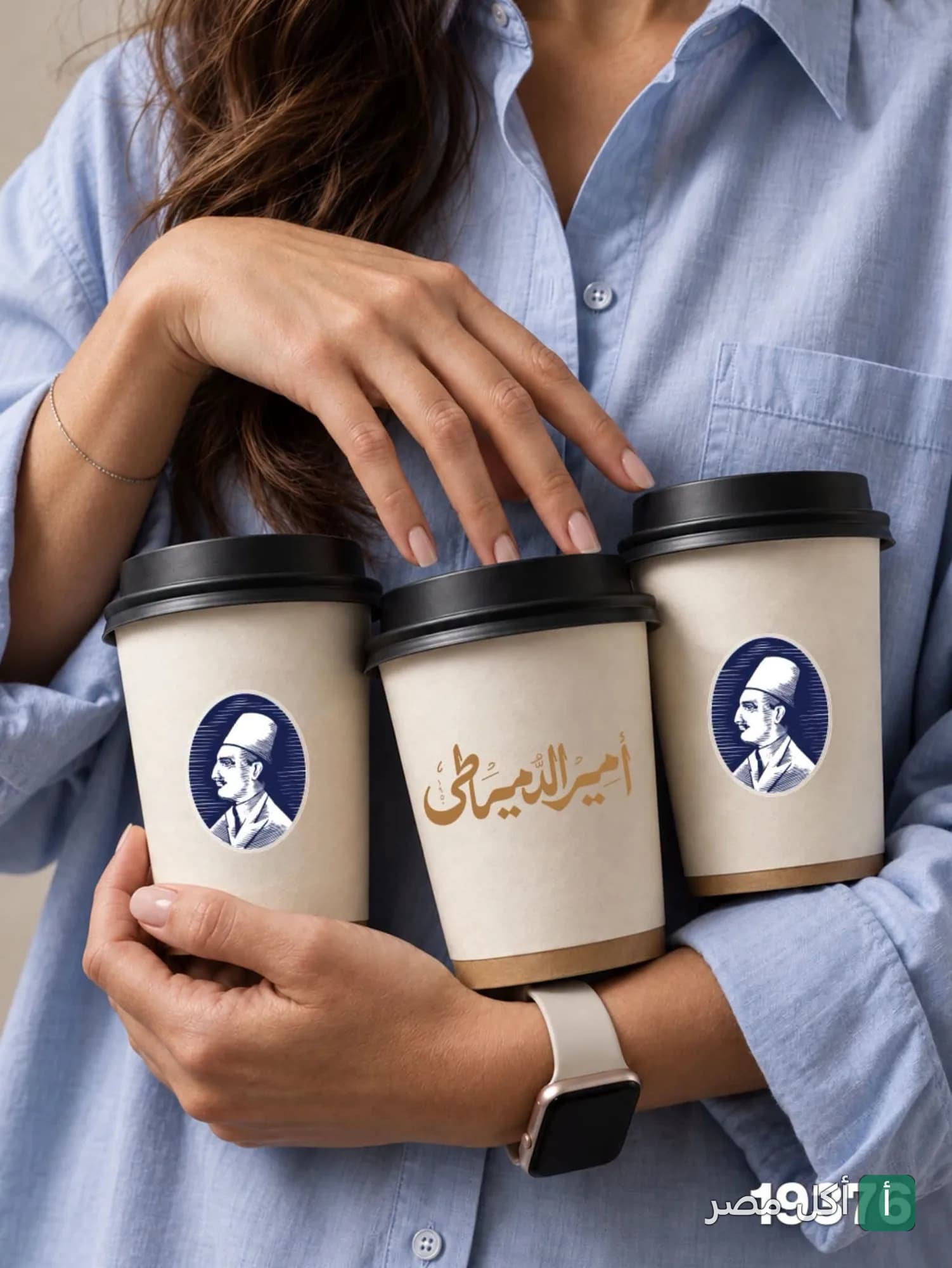 شخص يحمل ثلاثة أكواب ورقية تحمل شعار واسم مطعم الدمياطي للحلويات.