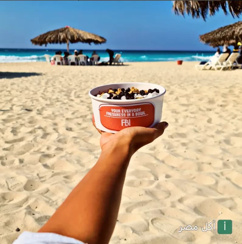 يد تحمل وعاء من FBI Cafe على شاطئ البحر في برج العرب.
