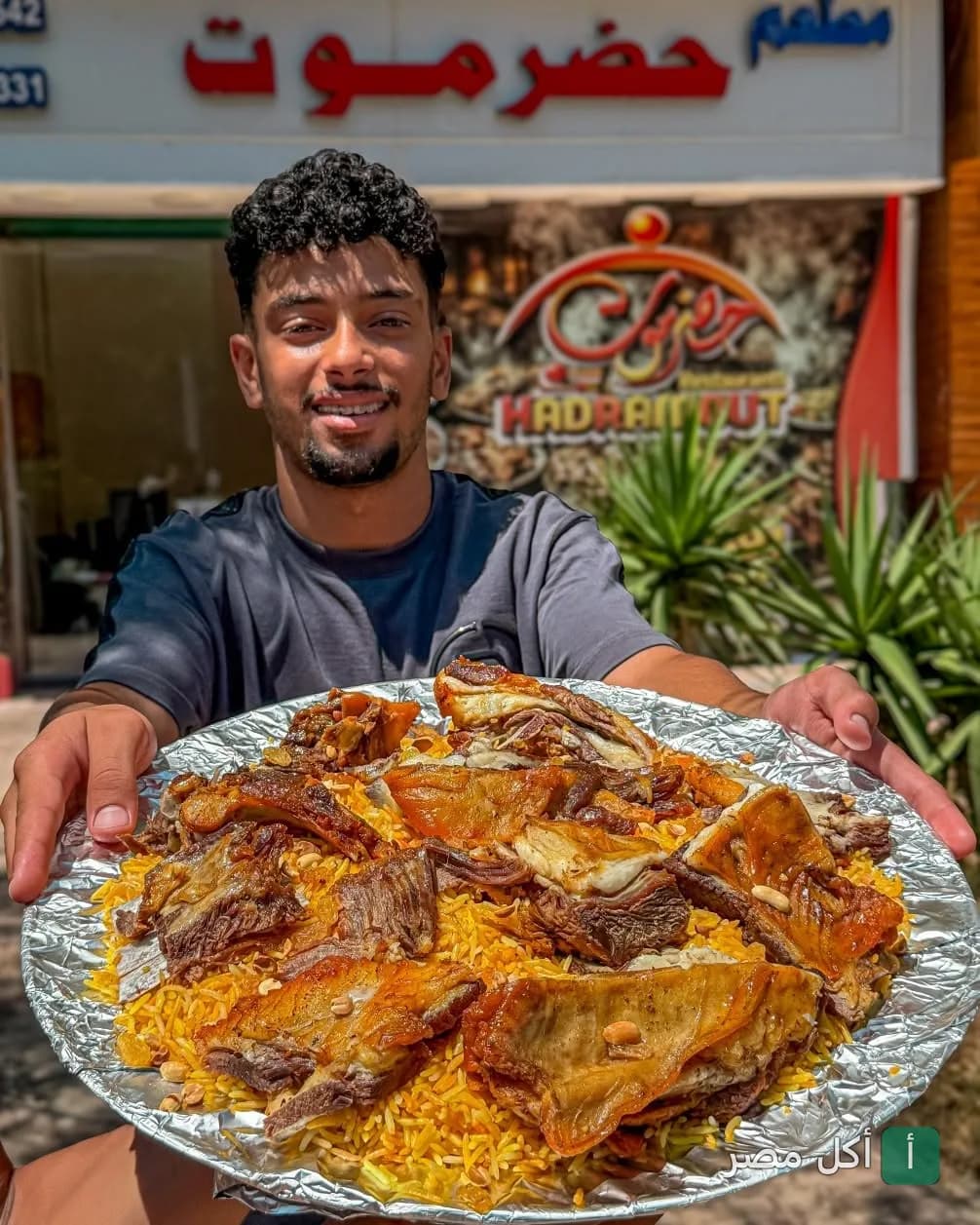 شاب يحمل صينية كبيرة من الأرز باللحم أمام واجهة مطعم حضرموت في كرموز بالإسكندرية.