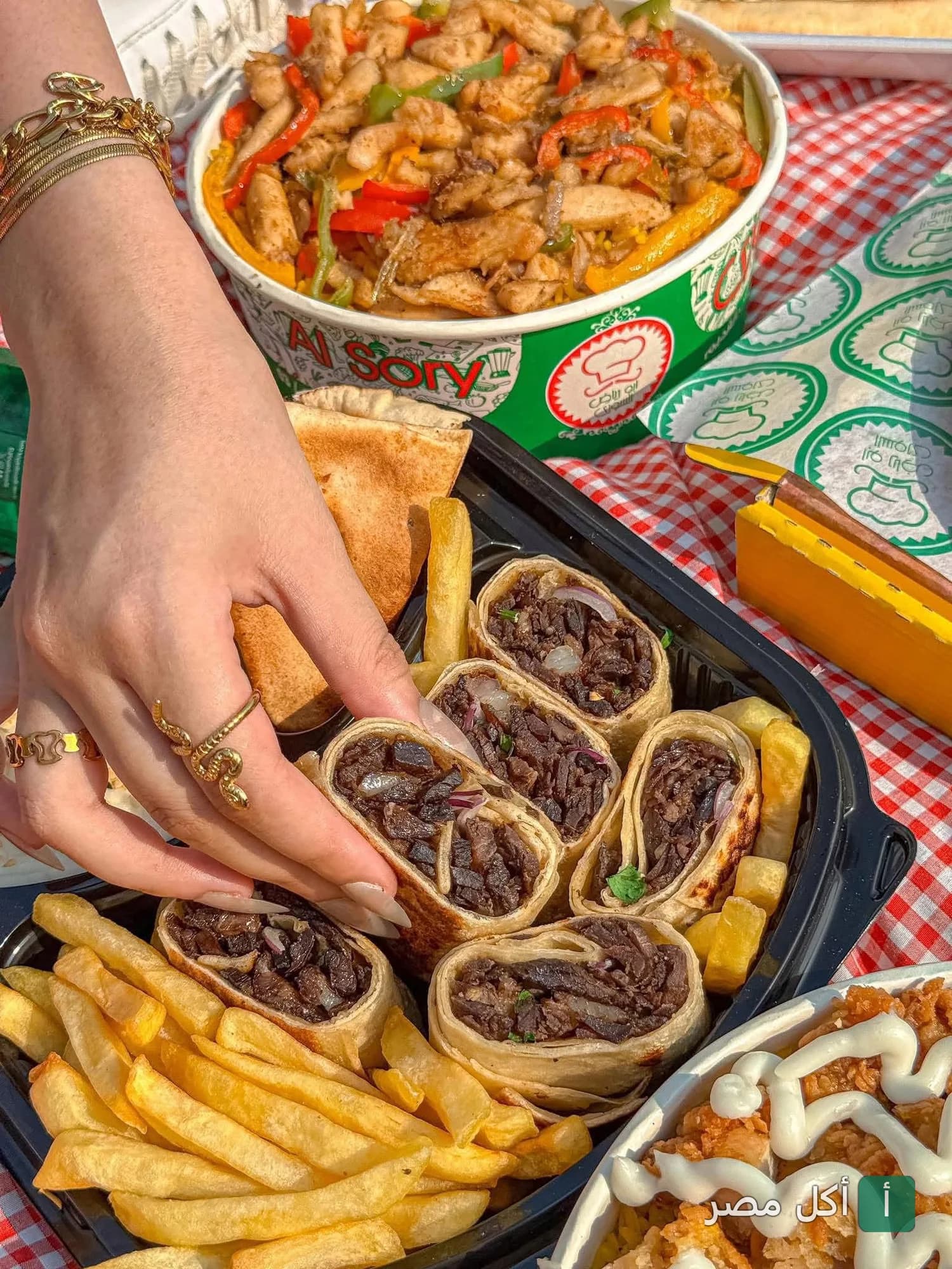 يد تمسك قطعة شاورما لحم مقطعة من وجبة مطعم ابو رياض السوري في كرموز مع بطاطس مقلية وأرز بالدجاج.
