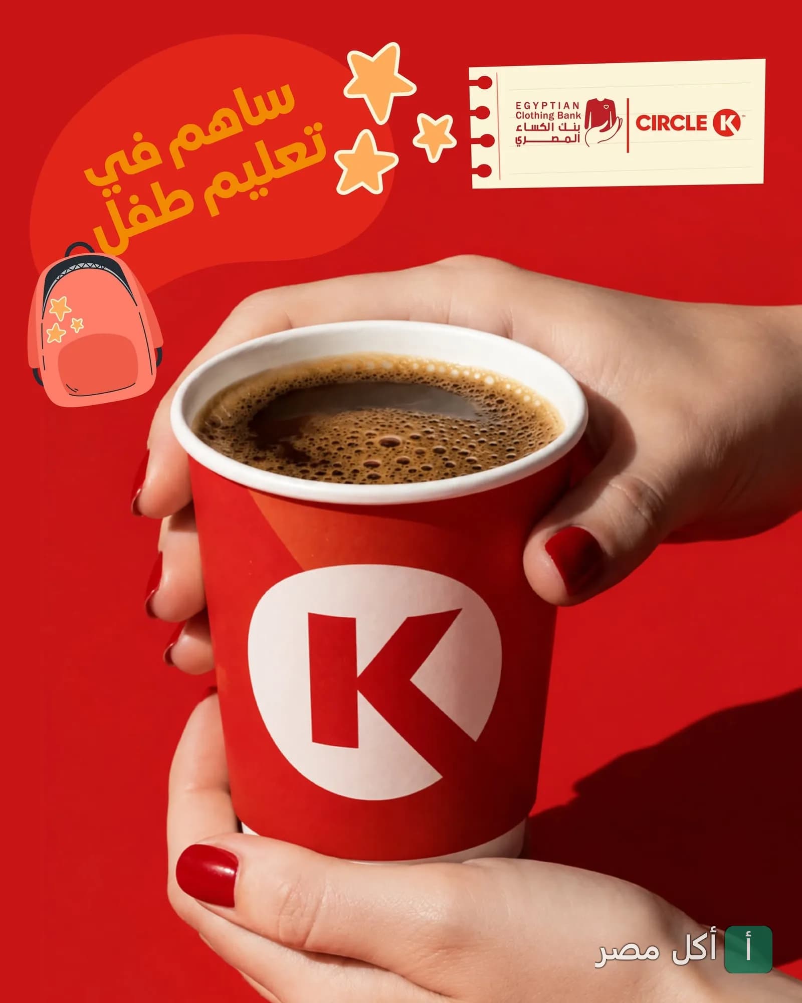يد تمسك كوب قهوة أحمر يحمل شعار سيركل كيه في حملة خيرية لدعم تعليم الأطفال.
