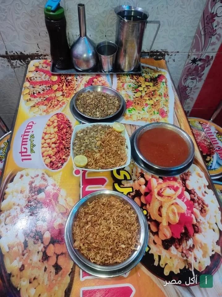 طاولة طعام في مطعم كشري الحسيني في مينا البصل بالإسكندرية عليها أطباق الكشري والصلصة.