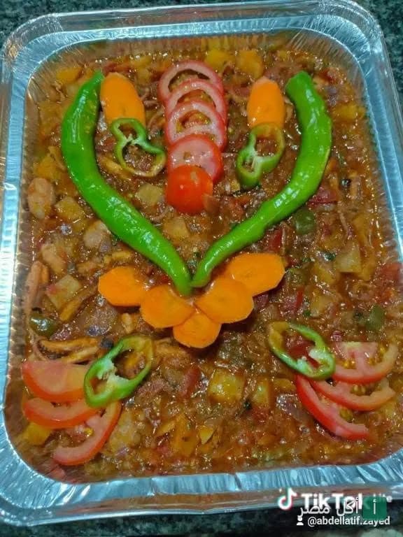 طبق مأكولات شرقية مطبوخة في علبة ألومنيوم مزين بشرائح الطماطم والجزر والفلفل الأخضر من مطعم الفرسان.