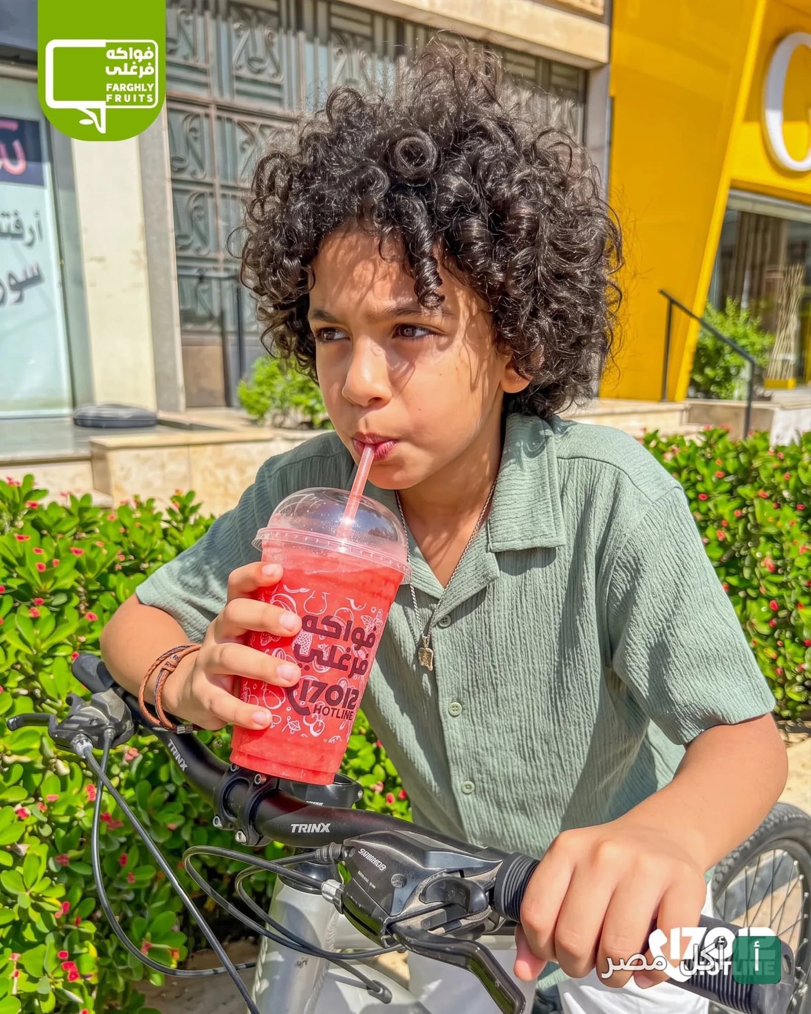 طفل يركب دراجة ويشرب عصير أحمر أمام كافيه الحاج علي فرغلي في مينا البصل بالإسكندرية.