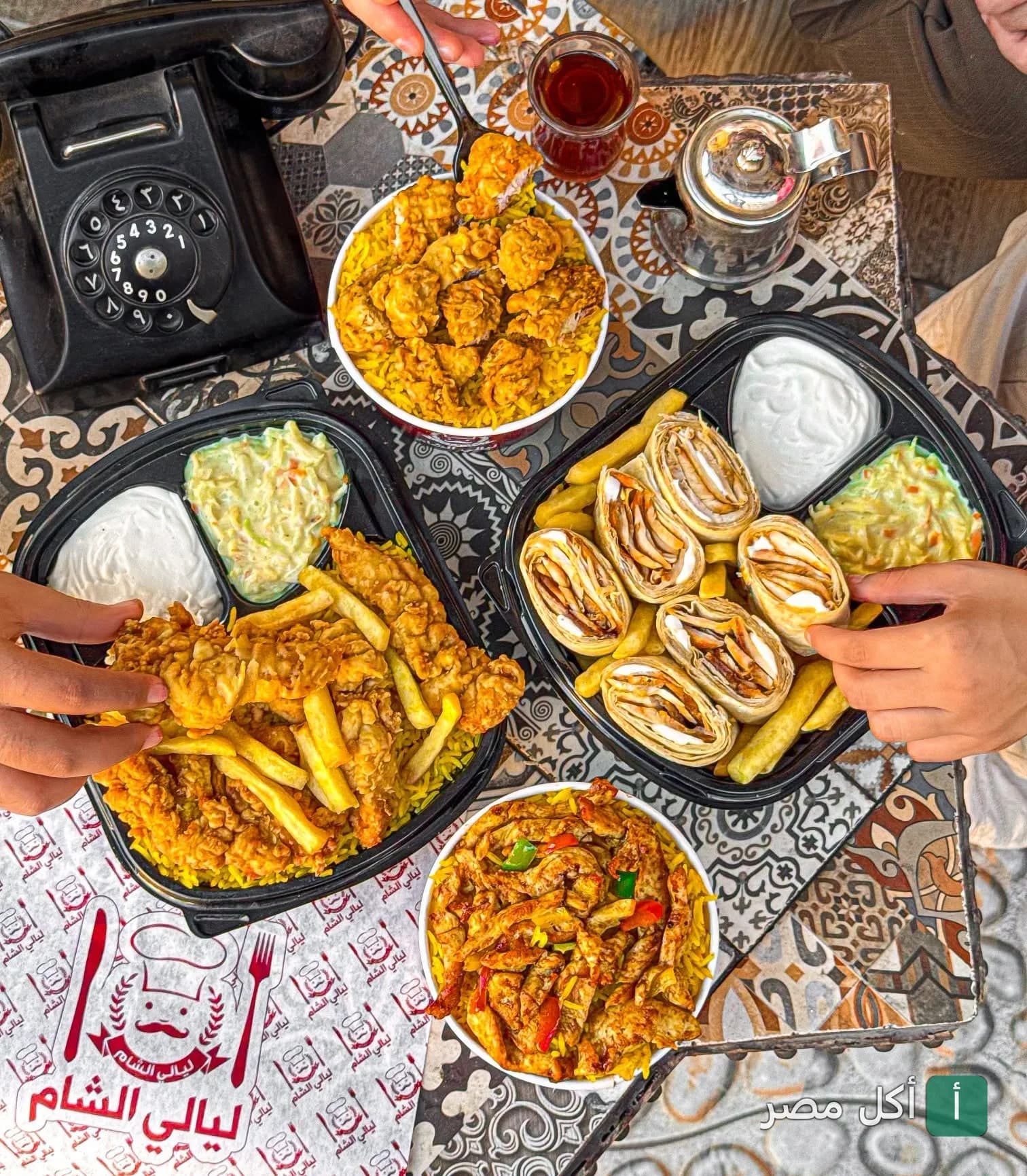 مائدة متنوعة من وجبات مطعم ليالي دمشق في مينا البصل، تشمل أطباق الدجاج المقرمش والشاورما مع المقبلات.