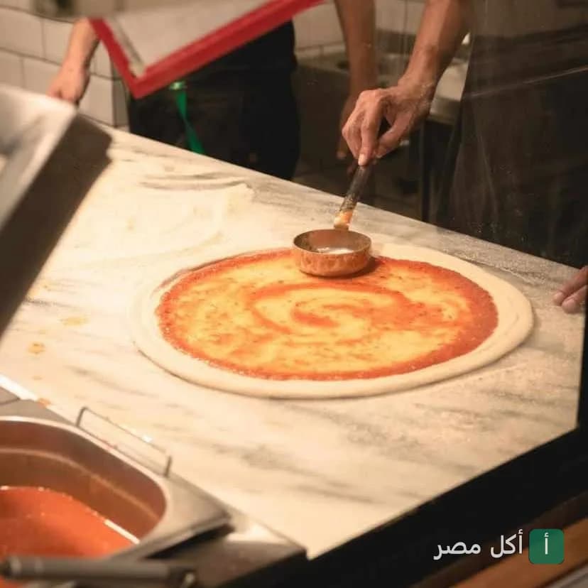 طباخ بيوزع صلصة الطماطم على عجينة البيتزا في كافية باب الحارة بمينا البصل.