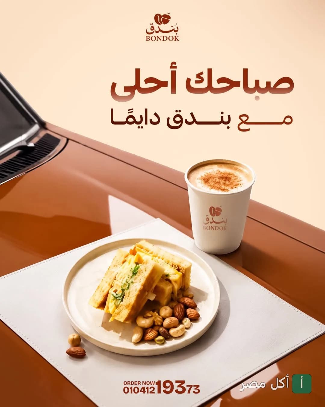 كوب قهوة وساندوتش مع مكسرات على غطاء سيارة في إعلان كافيه بندق بمينا البصل.
