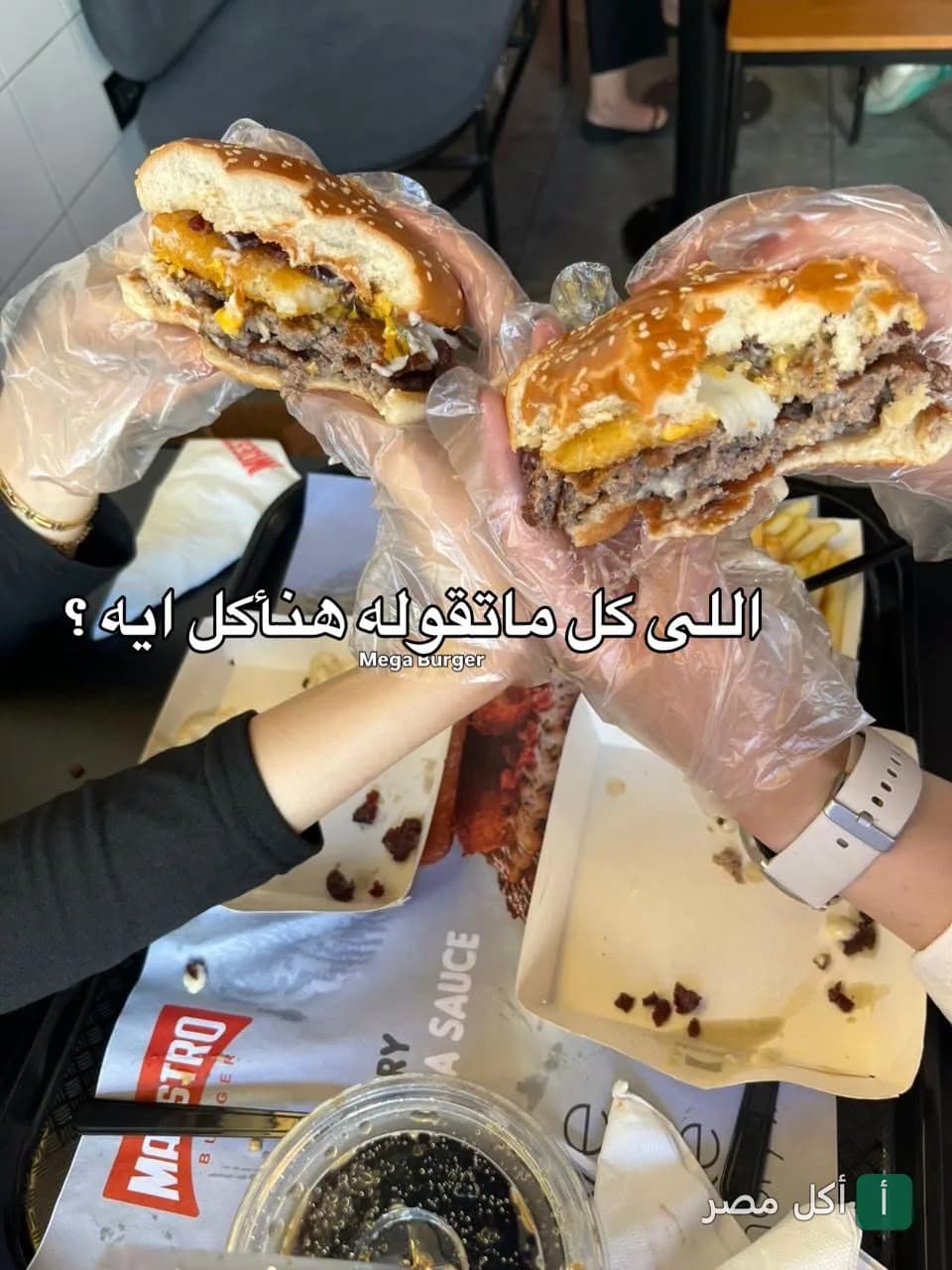 شخصان يمسكان شطائر برجر مزدوجة في مطعم المايسترو بمينا البصل في الإسكندرية.