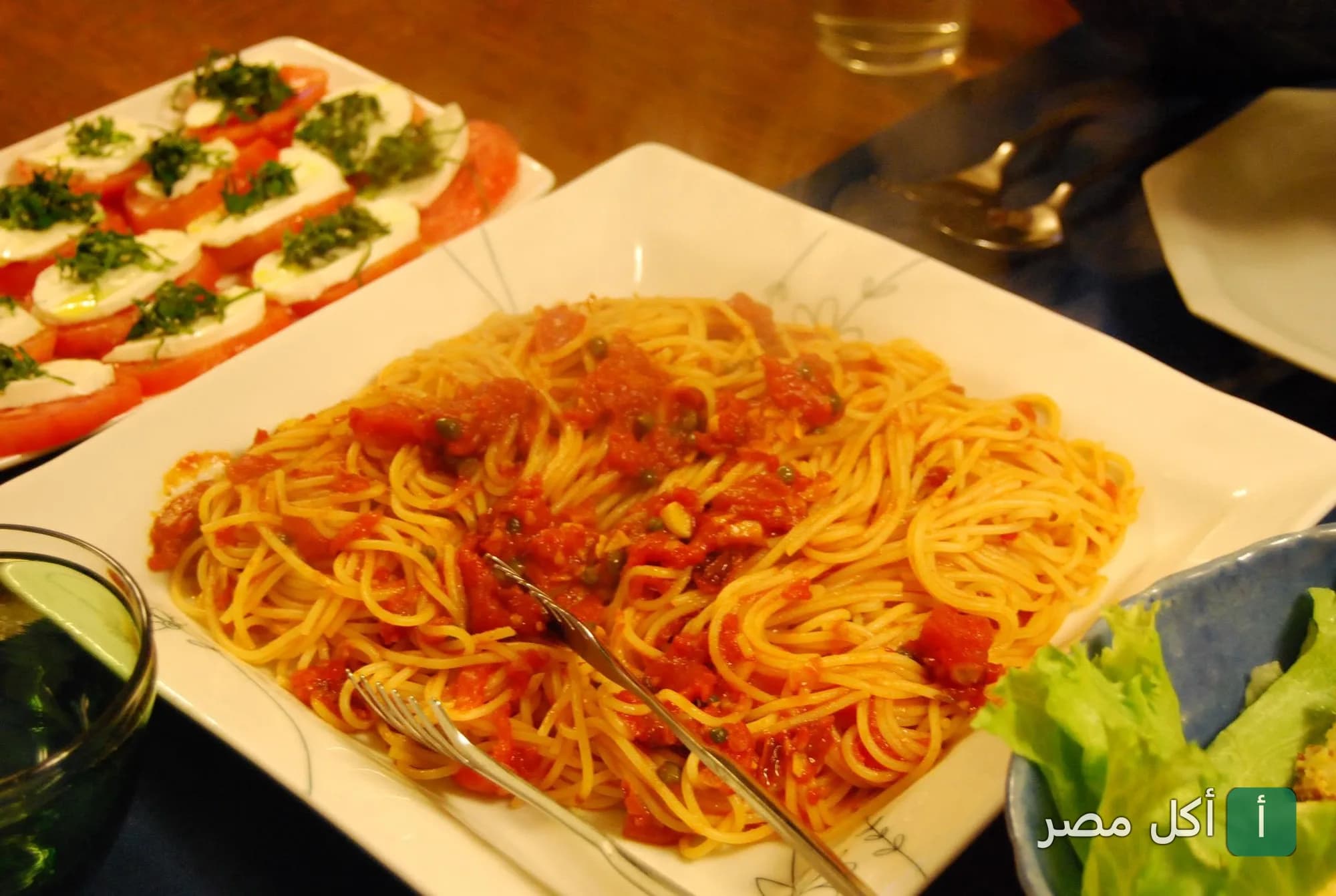 طبق مكرونة بصلصة الطماطم بجانبه طبق سلطة كابريزي في مطعم ميتو سكوير بالمنتزة.